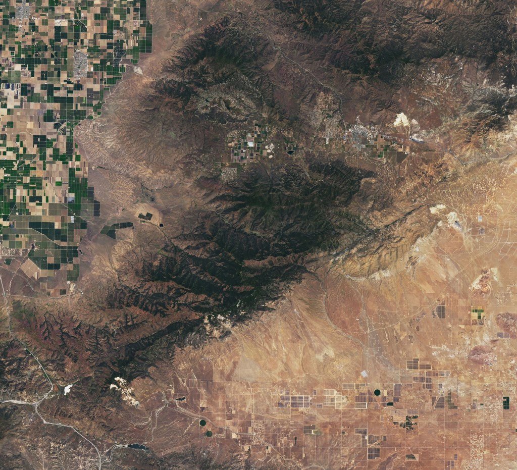 Satellite image of the Tehachapi Mountains showing forested ridges, dry valleys, and agricultural fields at the edge of the Central Valley